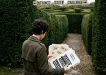 Person in trench coat holding folders labeled redacted standing at maze entrance